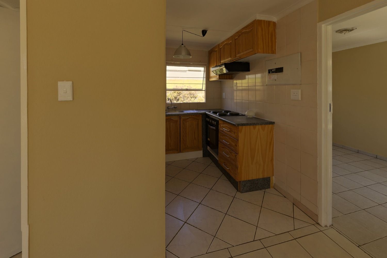 Empty kitchen with wood cabinets, a tiled backsplash, a gas range and a tiled floor, seen through a doorway, before virtual staging