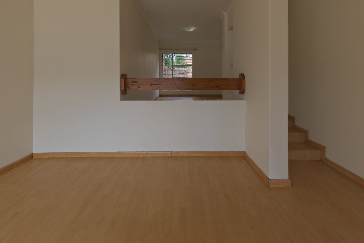 Empty living room with white walls, a wood floor, a staircase and a half wall with a wooden rail, before virtual staging